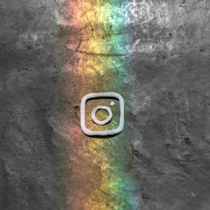 An Instagram logo etched into a dark, textured surface with a colorful rainbow light beam, announcing their new feature to combat bullying, illuminating the logo.