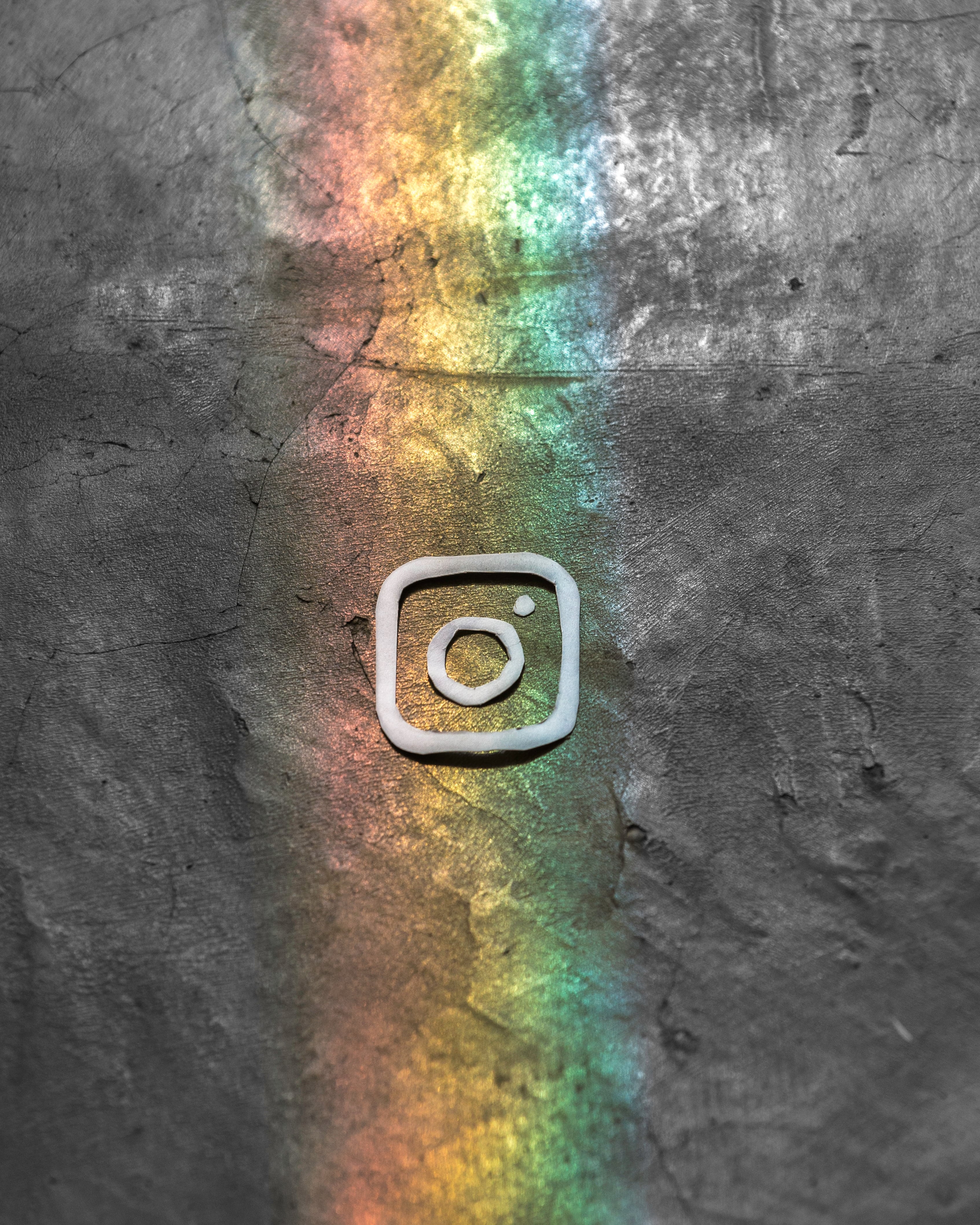 An Instagram logo etched into a dark, textured surface with a colorful rainbow light beam, announcing their new feature to combat bullying, illuminating the logo.