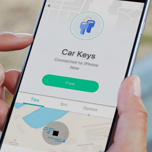 A person holds a smartphone displaying an app interface labeled "Car Keys," connected to the iPhone via Bluetooth beacon. The screen features buttons such as "Find," "Tips," "Siri," and "Option." A partial map is visible at the bottom, showcasing Apple's sleek product design.