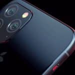 Close-up view of the back of an iPhone 11 displaying its triple-camera system and a shiny Apple logo. The phone's sleek black finish is highlighted by the surrounding lighting, with a hint of red accent on the side. The background is black, capturing the elegance predicted by Bloomberg for Apple's September event.