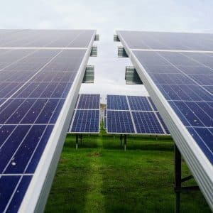 Close-up view of solar panels aligned in rows on a green grassy field in Taiwan, with a cloudy sky in the background. The image captures the perspective between two rows of panels, emphasizing solar energy as a clean, renewable source.