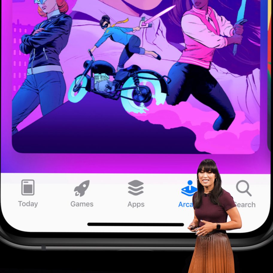 A woman stands on stage in front of a large screen displaying a stylized illustration on a mobile device. The illustration features animated characters in action poses, including a person on a motorcycle and another holding a weapon. The mobile device shows various app icons at the bottom.