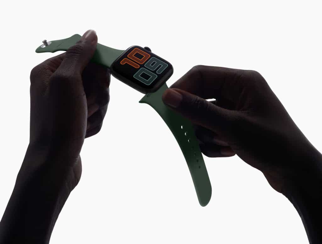 A person is holding a green Apple Watch Series 5 with a large digital display showing the time "10:09". The watch has a rectangular face and a green strap. The background is white, highlighting everything you need to know about this stylish accessory.