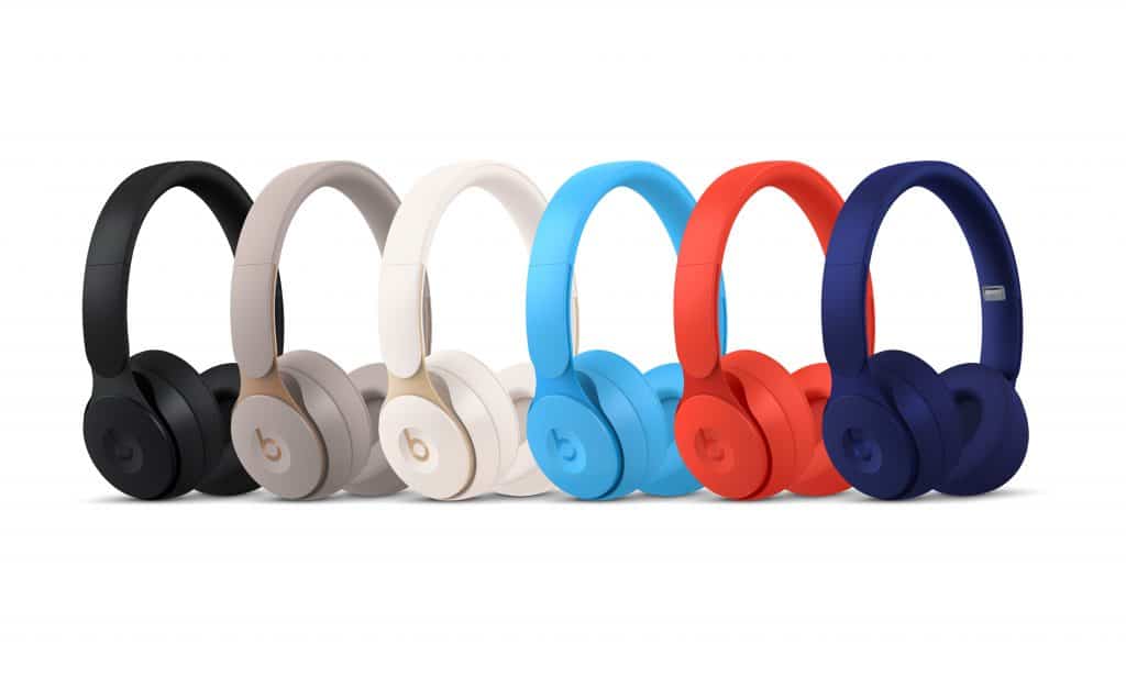 A row of six Beats Solo Pro headphones in different colors—black, grey, white, light blue, red, and dark blue—are arranged side by side on a white background. Each Apple headphone features the signature 'b' logo on the ear cups.