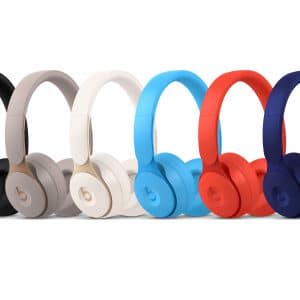 A row of six Beats Solo Pro headphones in different colors—black, grey, white, light blue, red, and dark blue—are arranged side by side on a white background. Each Apple headphone features the signature 'b' logo on the ear cups.