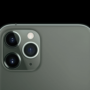 Close-up view of the top rear section of an iPhone 11 Pro Max featuring a metallic finish and a triple camera setup. The three camera lenses and a flash are arranged in a triangular pattern. The background is solid black, making the phone's design stand out, as highlighted by Consumer Reports' best smartphone ranking.