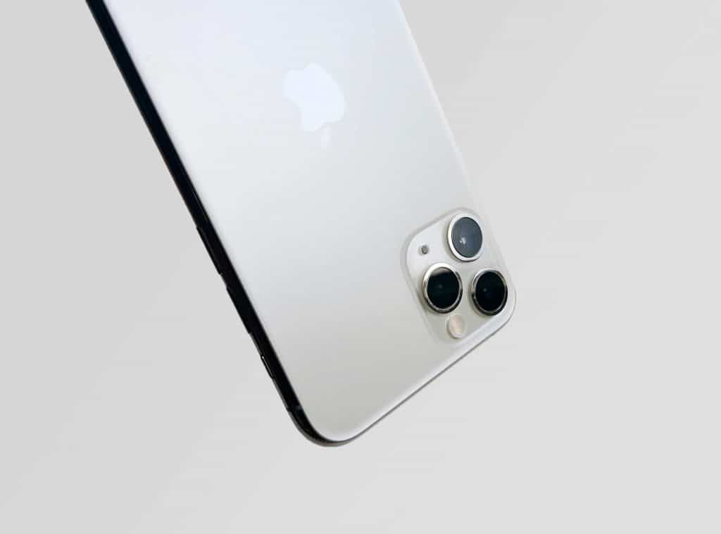 Close-up of the backside of a silver smartphone with a prominent camera module housing three lenses and a flash, set against a white background. The phone, featuring the iPhone logo of a well-known tech company, boasts cutting-edge 5G capabilities for enhanced connectivity.