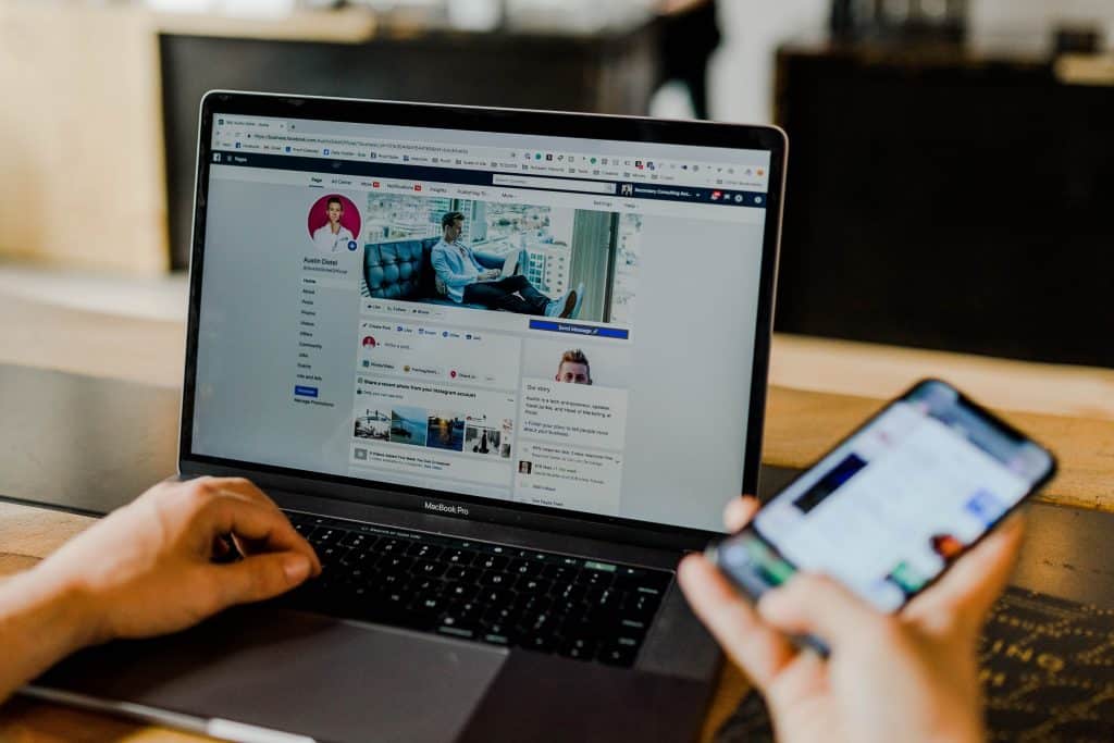 A person is sitting at a desk, using a laptop displaying a social media profile. One of their hands is on the laptop's keyboard, while the other hand holds a smartphone with another social media screen. The background is slightly blurred, reflecting some of the biggest developments in connectivity since 2019.