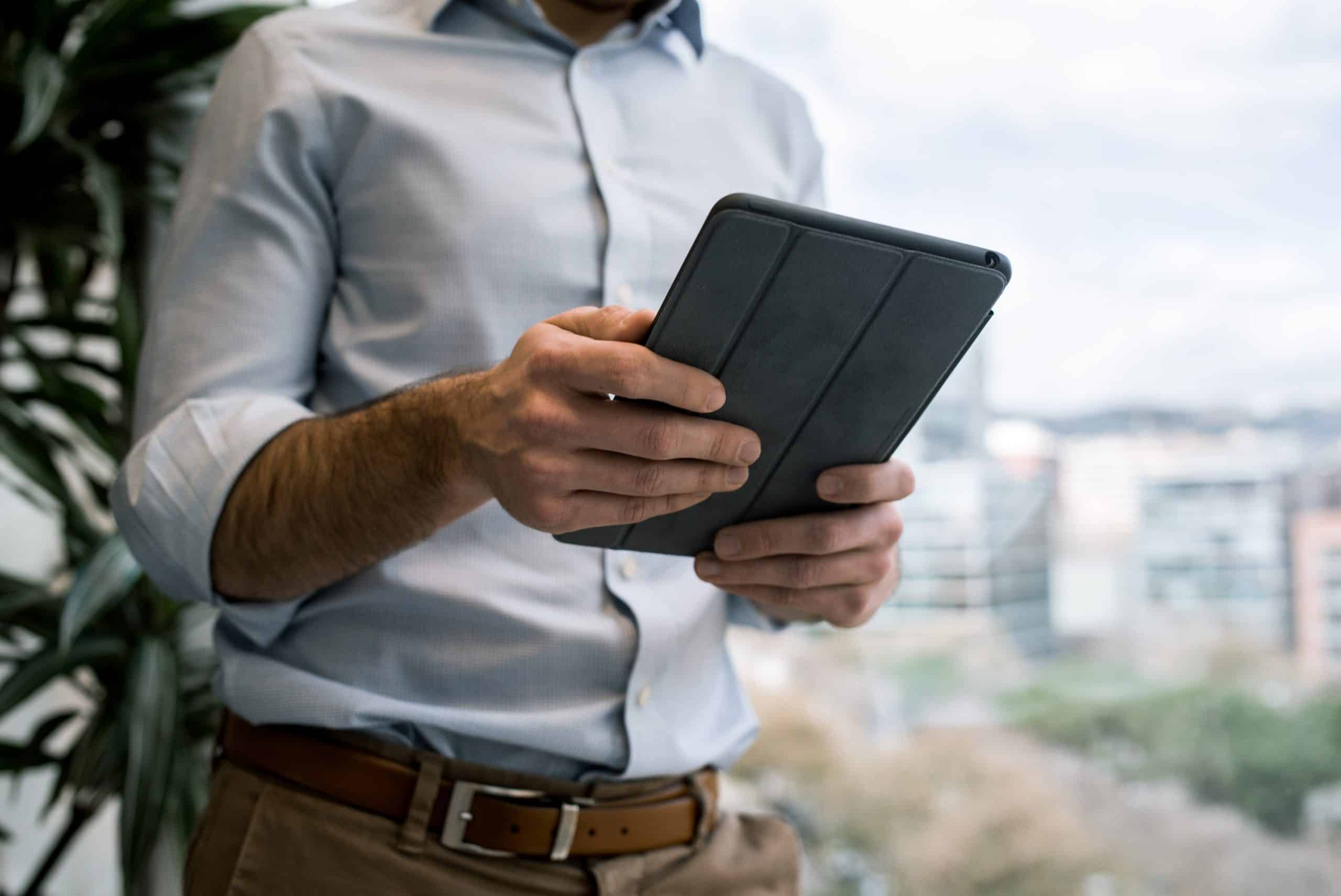 A person in a light blue shirt, possibly the CEO, holds a tablet device with both hands. The background features an office setting with large windows overlooking a blurred cityscape. A plant is visible on the left side, and it looks like they might be using the Instagram iPad app.