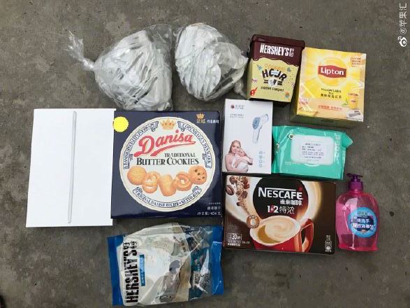 A collection of items arranged on the ground, including two wrapped bread loaves, Hershey's Kisses chocolates, Lipton tea, Danisa butter cookies, a pen, facial mask, Nescafé coffee sachets, wet wipes, and a bottle of hand soap—ideal for thoughtful care packages for employees in China.