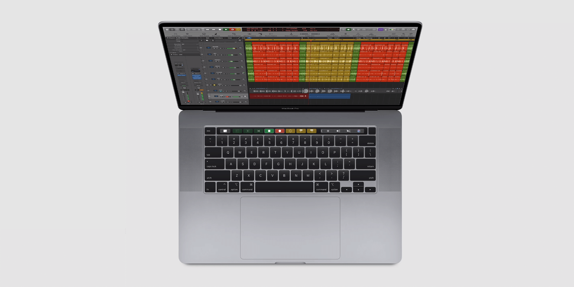 A top view of a silver MacBook Pro laptop with a Logic Pro music production interface open on the screen. The interface displays multiple audio tracks in different colors. Like many Macs, the laptop features a keyboard with a Touch Bar above it and a large trackpad.