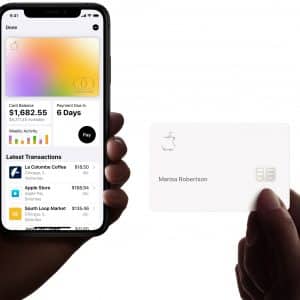 A person holds an iPhone displaying a credit card management app, showing a balance of $1,862.25 and recent transactions, including a missed March payment. Another hand holds a physical Apple Card with the name "Marisa Robertson" and the Apple logo.
