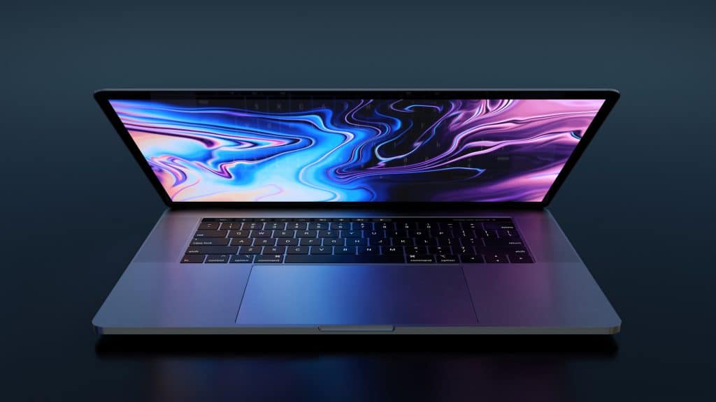 A sleek, open laptop on a dark surface displays an abstract, colorful, and swirling digital background. The laptop has a backlit keyboard and a reflective screen, casting a soft glow that complements the vibrant hues of the display—making it an ideal addition to any tech wishlist before the release of macOS 10.16.