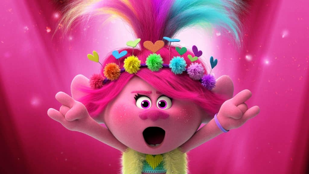 A colorful animated character with bright pink skin, vibrant pink hair, and a flower and heart headband stands against a pink backdrop. Released by Universal Pictures, the character has a surprised expression with open mouth and raised hands.