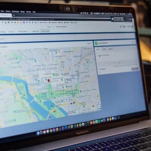 A MacBook Pro laptop screen displays a map of Washington, D.C., with a red location pin marking a specific area. Various desktop objects, including a baseball, are partially visible in the background. The browser window shows navigation and search options, possibly for US officials or tech giants.