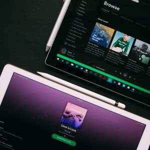 A tablet displaying the album "Love is Love" with the Spotify interface and another device with the Spotify browse page open, both placed on a dark surface with a stylus near each device—a perfect setup for exploring global music streaming options.