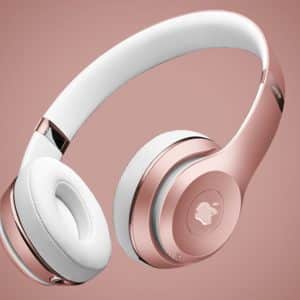 A pair of over-ear headphones with metallic rose gold and white accents. The headband and ear cushions are white, while the outer parts of the ear cups and parts of the headband are rose gold. Reminiscent of Apple's new AirPods Studio, the background features a gradient of pink hues.