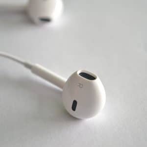 Close-up image of a white Apple EarPod marked with an "R" to indicate it is for the right ear, designed specifically for iPhones. Another EarPod is slightly out of focus in the background, both resting on a clean white surface.