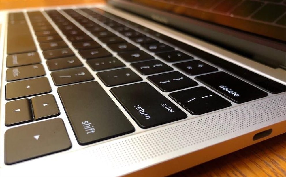 Design novelty - Close-up image of the keyboard of a MacBook laptop. The focus is on the left side, showing keys like shift, tab, caps lock, and return. The edge of the screen and the laptop’s hinge are also partially visible against a wooden surface—a familiar sight for many programmers.