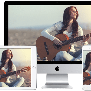 A woman playing an acoustic guitar is displayed on an iMac, iPad, iPhone, and iPod touch, illustrating wirelessly streaming media across multiple Apple devices. The woman is outdoors, possibly on a beach, wearing a white long-sleeve top and blue jeans.