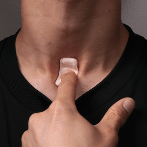 A person wearing a black shirt touches a small, skin-colored adhesive patch on their throat, a cutting-edge wearable device designed to diagnose coronavirus.