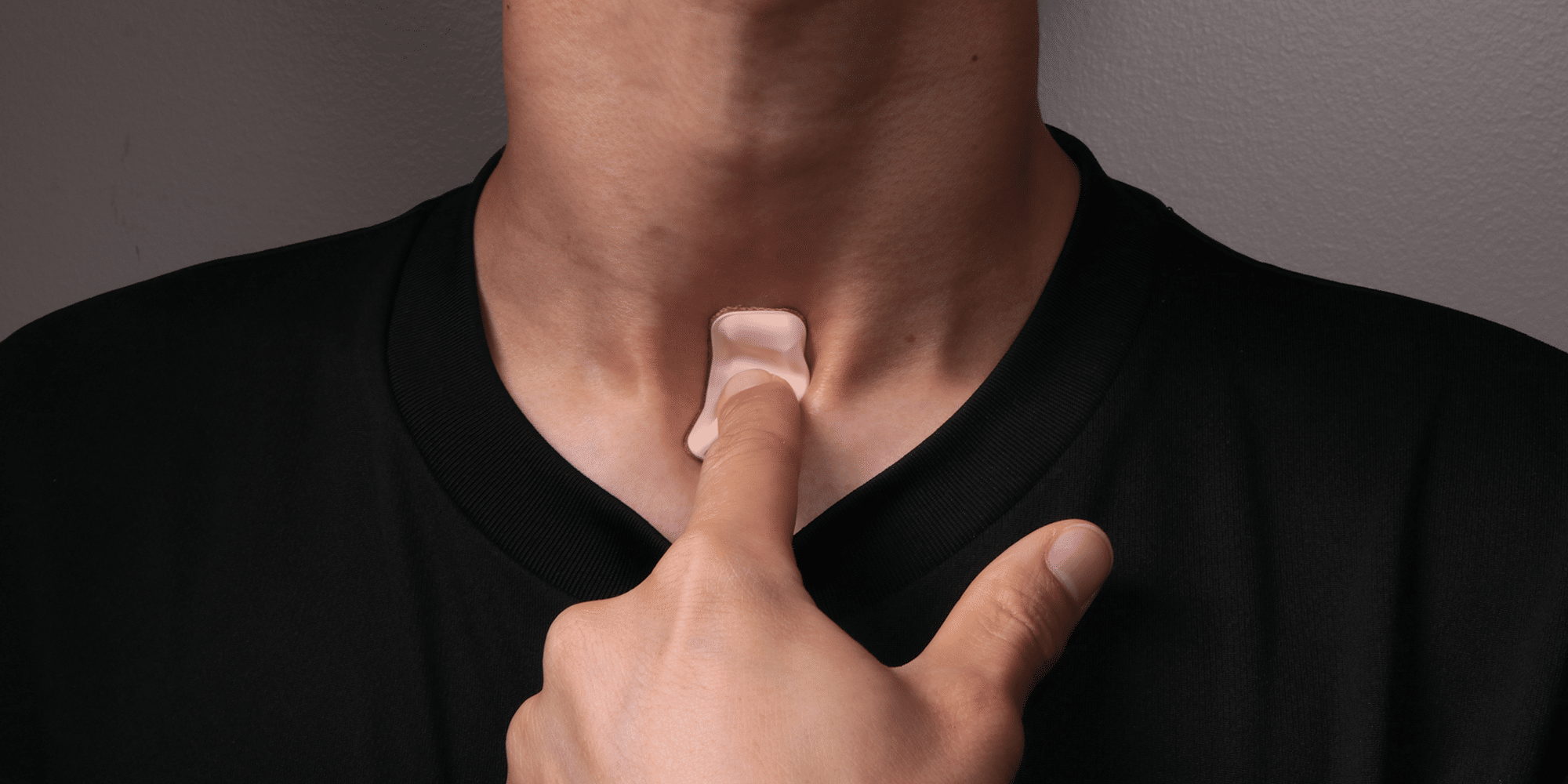 A person wearing a black shirt touches a small, skin-colored adhesive patch on their throat, a cutting-edge wearable device designed to diagnose coronavirus.