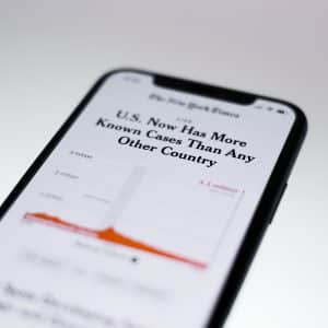 A smartphone displaying a news article from Apple News with the headline "U.S. Now Has More Known Cases Than Any Other Country." The article, originally from The New York Times, includes a graph showing a peak in COVID-19 cases at the 3.3 million mark.