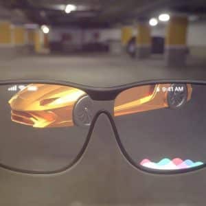 Image of smart glasses displaying an augmented reality interface by iDrop News. The glasses screen shows a sleek orange sports car and a colorful icon bar at the bottom, reminiscent of Apple’s design ethos. In the background, a dimly lit parking garage enhances the futuristic vibe, akin to previewing an iPhone 12 with Apple Glass.