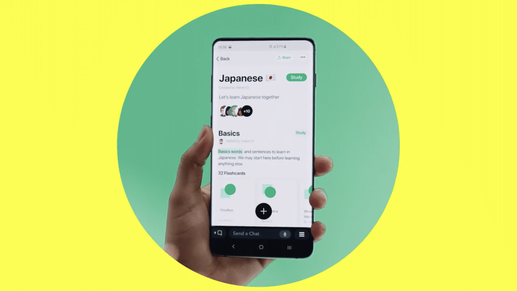 A hand holds a smartphone displaying a language learning app. The screen shows a Japanese course named "Basics" with various study options like flashcards, rivaling popular platforms. The background is a split of bright yellow and green, reminiscent of Snapchat's vibrant palette.