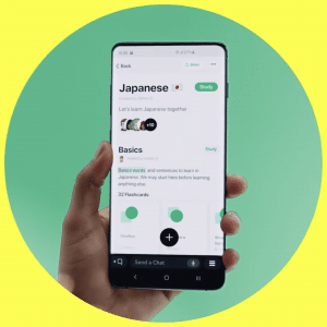 A hand holds a smartphone displaying a language learning app. The screen shows a Japanese course named "Basics" with various study options like flashcards, rivaling popular platforms. The background is a split of bright yellow and green, reminiscent of Snapchat's vibrant palette.