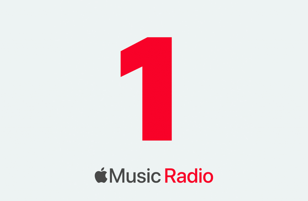 An image features a large, red numeral "1" in the center against a light grey background. Below the numeral, the text reads "Apple Music 1" with the Apple logo preceding the words "Music Radio," highlighting one of Apple Music’s new radio stations.