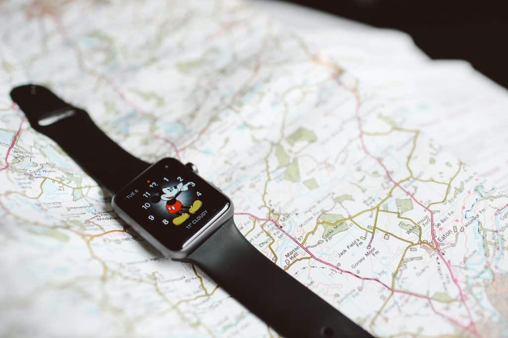 A smartwatch with a Mickey Mouse watch face displaying the time is placed on a detailed paper map. The watch has a black band, and the map features roads, landmarks, and various geographic details of Ireland.