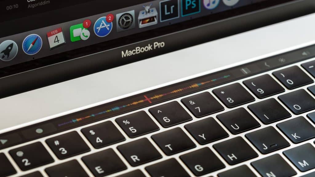 Image of an Apple MacBook Pro laptop keyboard with a close-up view of the Touch Bar displaying various icons. The screen shows a portion of the dock with applications such as Safari, Finder, and System Preferences, highlighting tools essential for protecting your Mac against viruses.