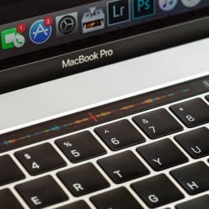 Image of an Apple MacBook Pro laptop keyboard with a close-up view of the Touch Bar displaying various icons. The screen shows a portion of the dock with applications such as Safari, Finder, and System Preferences, highlighting tools essential for protecting your Mac against viruses.