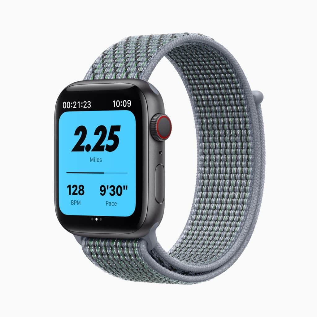 A smartwatch with a rounded square display shows workout metrics including time, distance (2.25 miles), heart rate (128 BPM), and pace (9'30"). It has a fabric loop band with shades of grey and is worn around the wrist.