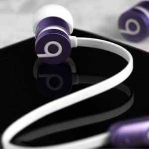 Close-up of a pair of purple and white in-ear Beats earphones—the best wired headphones— with their wire laying over a black smartphone. The earphones and phone sit on a marbled surface. The Beats logo is visible on the earphone buds.