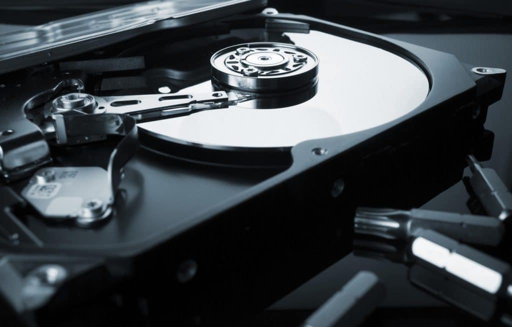 Close-up of an opened hard disk drive (HDD) showing the platters, spindle, actuator arm, and read/write head components. The drive's reflective surface contrasts with the sleek metallic parts, highlighting the intricate mechanics of data storage technology vital for tasks like recover deleted partition work.