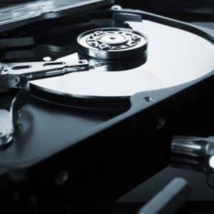 Close-up of an opened hard disk drive (HDD) showing the platters, spindle, actuator arm, and read/write head components. The drive's reflective surface contrasts with the sleek metallic parts, highlighting the intricate mechanics of data storage technology vital for tasks like recover deleted partition work.