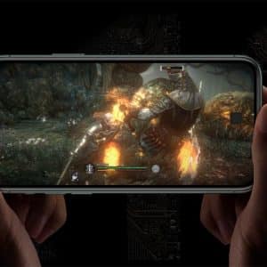 Hands holding a smartphone horizontally display an action scene from a mobile game. The screen shows a knight fighting a large monster with fire effects. The background is dark with abstract circuitry patterns, capturing the essence of modern mobile gaming on an Apple device.