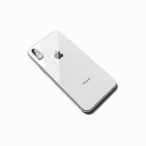 A silver iPhone with a dual-camera setup on the back, lying face down on a white surface. The Apple logo is visible in the center, and "iPhone" is printed near the bottom. The phone has a shiny, reflective surface, featuring Apple's new tracking feature for enhanced security.