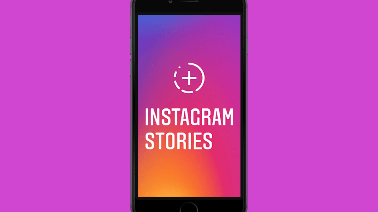 A smartphone displays the Instagram Stories screen, featuring a colorful gradient background transitioning from purple to orange, with a circular plus icon above the text "Instagram Stories." The phone is set against a bright purple background, highlighting Instagram's seamless cross-posting feature with Facebook.