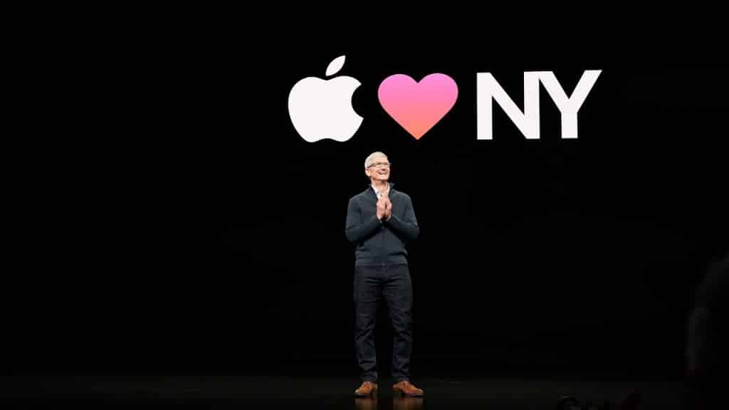 A person stands on a stage with a black background. Behind them, a large projected image displays the Apple logo, a heart symbol, and "NY," illustrating "Apple loves New York." Despite the challenges of the COVID-19 pandemic, Apple remains an intimate brand closely connected to its audience.