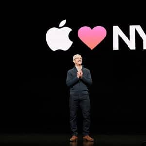 A person stands on a stage with a black background. Behind them, a large projected image displays the Apple logo, a heart symbol, and "NY," illustrating "Apple loves New York." Despite the challenges of the COVID-19 pandemic, Apple remains an intimate brand closely connected to its audience.