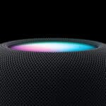 Close-up of a black Apple HomePod with Siri’s multicolor light glowing on the top display.