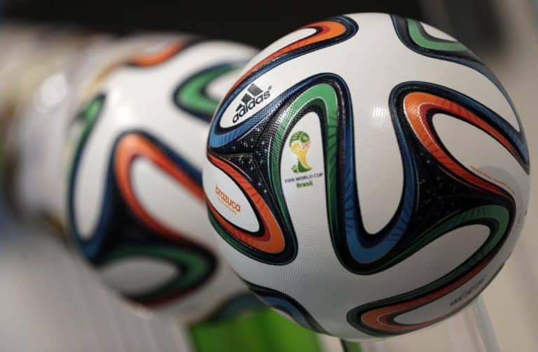 Close-up image of Adidas Brazuca soccer balls, the official match balls of the 2014 FIFA World Cup. They feature a white base with colorful swirling patterns in blue, orange, and green, showcasing the tournament logo and Adidas branding—highlights seen on TV rights broadcasts of major events like the FIFA Club World Cup.