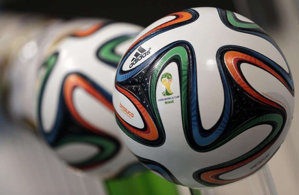 Close-up image of Adidas Brazuca soccer balls, the official match balls of the 2014 FIFA World Cup. They feature a white base with colorful swirling patterns in blue, orange, and green, showcasing the tournament logo and Adidas branding—highlights seen on TV rights broadcasts of major events like the FIFA Club World Cup.
