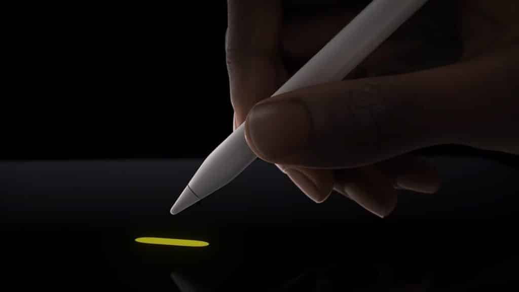 A hand holding a white Apple Pencil Pro is drawing a small yellow line on the latest iPads' touchscreen. The background is black, highlighting the illuminated line and stylus tip, showcasing the advanced features of this cutting-edge device.