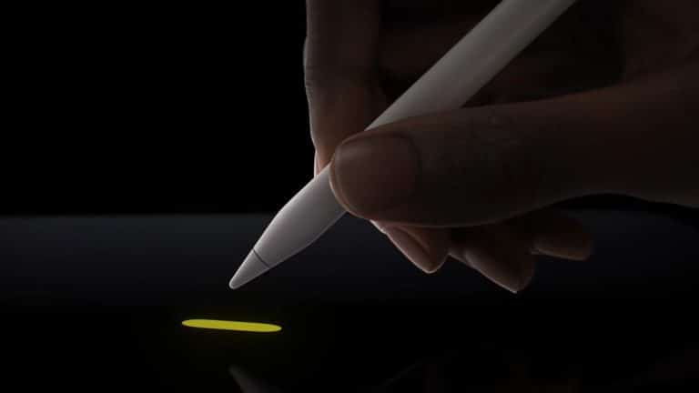 A hand holding a white Apple Pencil Pro is drawing a small yellow line on the latest iPads' touchscreen. The background is black, highlighting the illuminated line and stylus tip, showcasing the advanced features of this cutting-edge device.