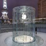 A cylindrical glass entrance featuring the Apple logo leads to an underground Apple Store in a cityscape with tall, illuminated buildings and the iconic Oriental Pearl Tower in the background at night. Amid a sales surge due to iPhone discounts in China, a few people are walking near the entrance.