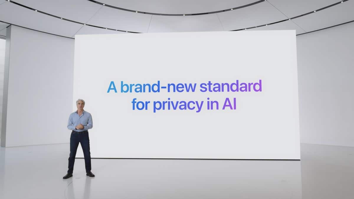 A person stands on a minimalist stage with an illuminated white background screen displaying the text "A brand-new standard for privacy in AI." The individual is casually dressed and presenting, with an arching ceiling and sleek design elements around them.